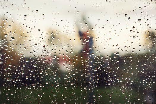 Rain droplets on glass with a blurred scenic background, creating a moody atmosphere.