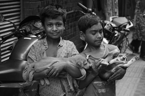 Grayscale Photo of Two Boys Carrying Puppies