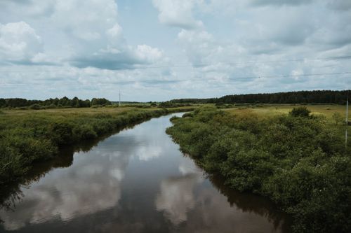 Free Tranquil river flowing through lush greenery under a cloudy sky, capturing nature's beauty. Stock Photo