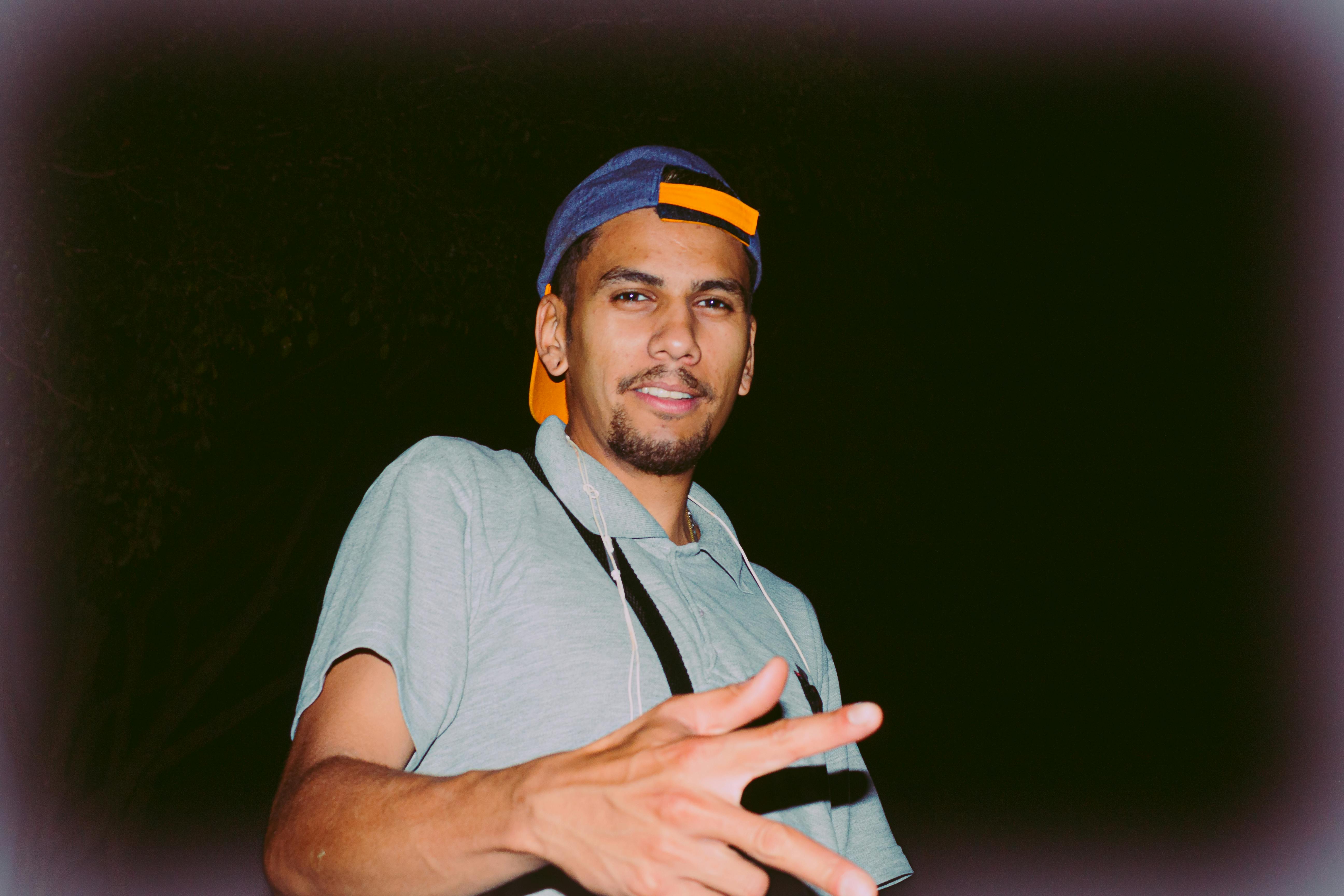 Man wearing a blue cap and gray polo shirt, smiling and posing outdoors at night.