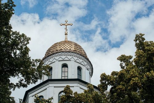 Free A splendid view of an Orthodox church dome adorned with golden cross, framed by trees under a blue sky. Stock Photo