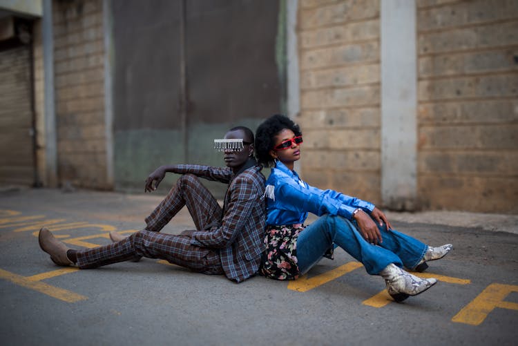 Models In Trendy Clothes Sitting On Ground On Street