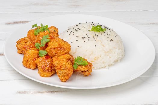 A close-up of crispy fried chicken with sesame rice garnished with fresh herbs on a white plate.