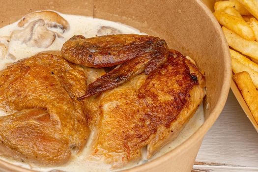 Savory roasted chicken with mushroom sauce in paper bowl, served with fries. Perfect comfort food.