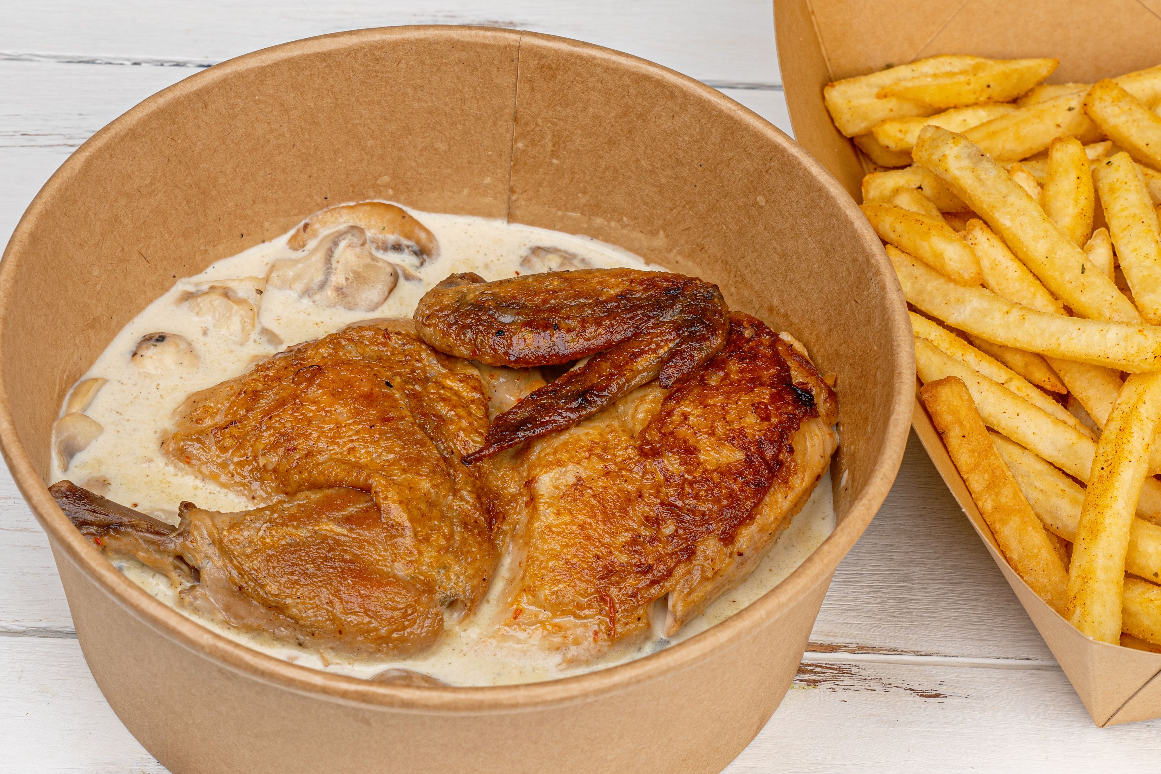 Delicious fried chicken with creamy mushroom sauce and crispy fries in takeaway containers.