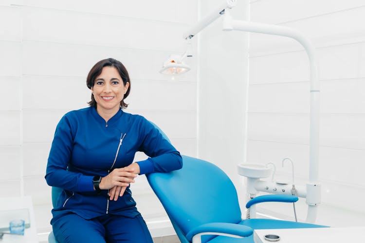 Woman In Blue Attire Sitting Beside Dental Chair