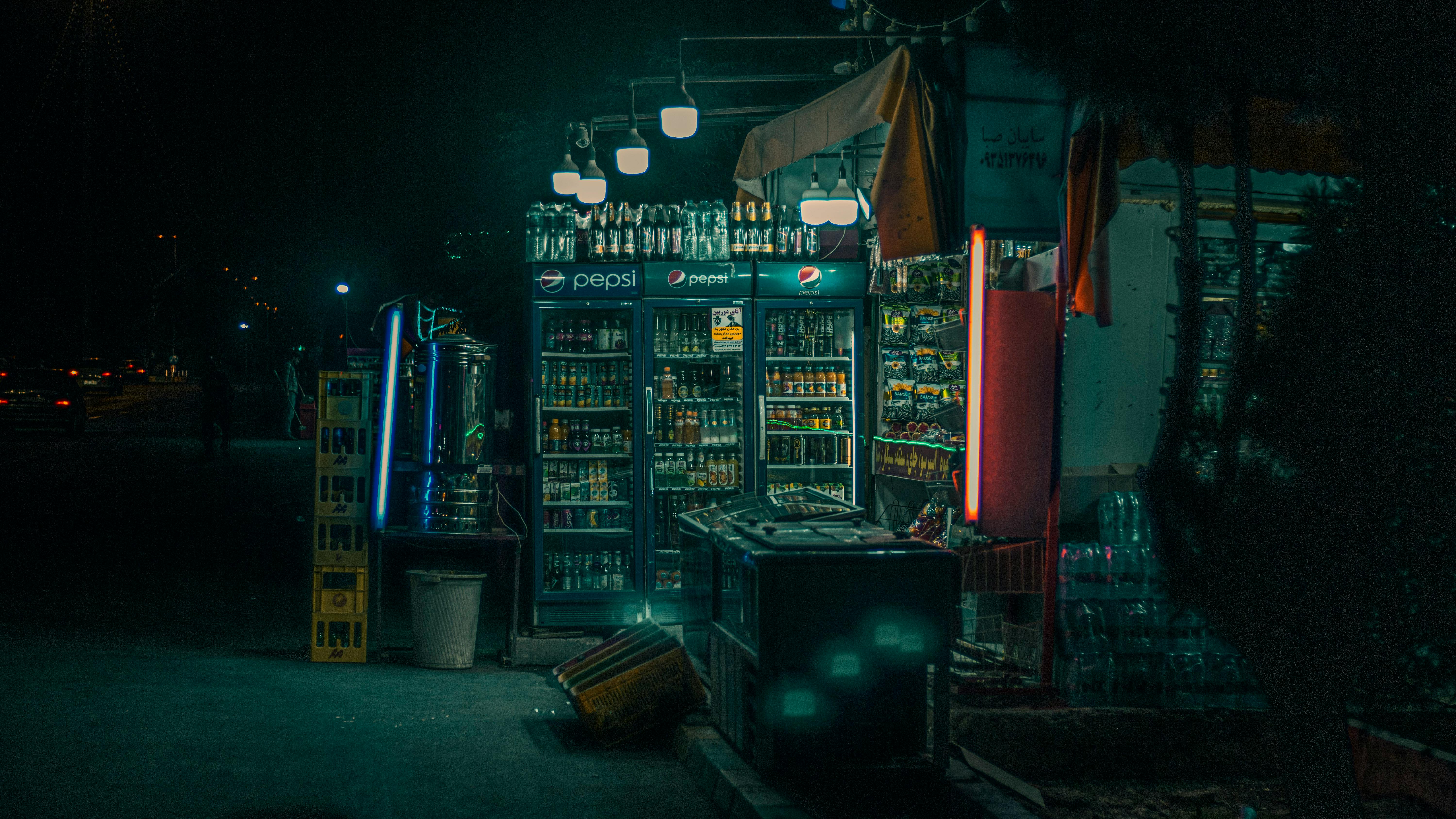Cozy night view of a street vendor with illuminated beverage fridges and inviting atmosphere.