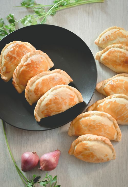Free Golden-brown empanadas served on a sleek black plate, surrounded by fresh shallots and greens. Stock Photo