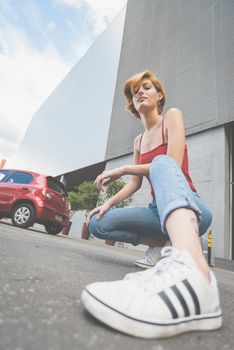 Fashionable young woman crouching on street in urban setting with modern architecture.