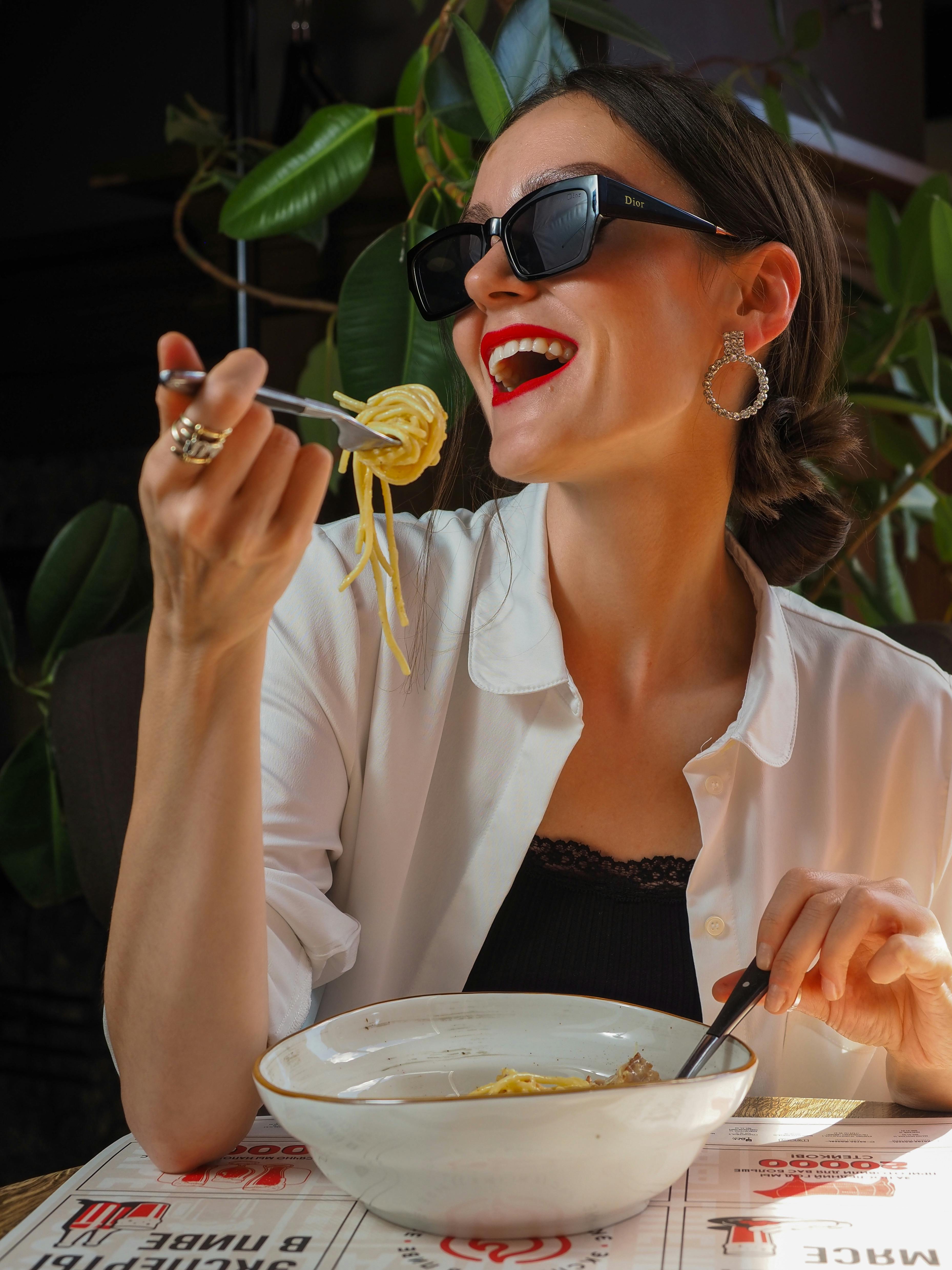 smiling woman eating pasta in restaurant