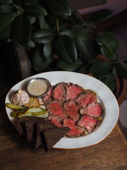 Delicious beef carpaccio platter with rye bread and dipping sauce, perfect for gourmet dining.