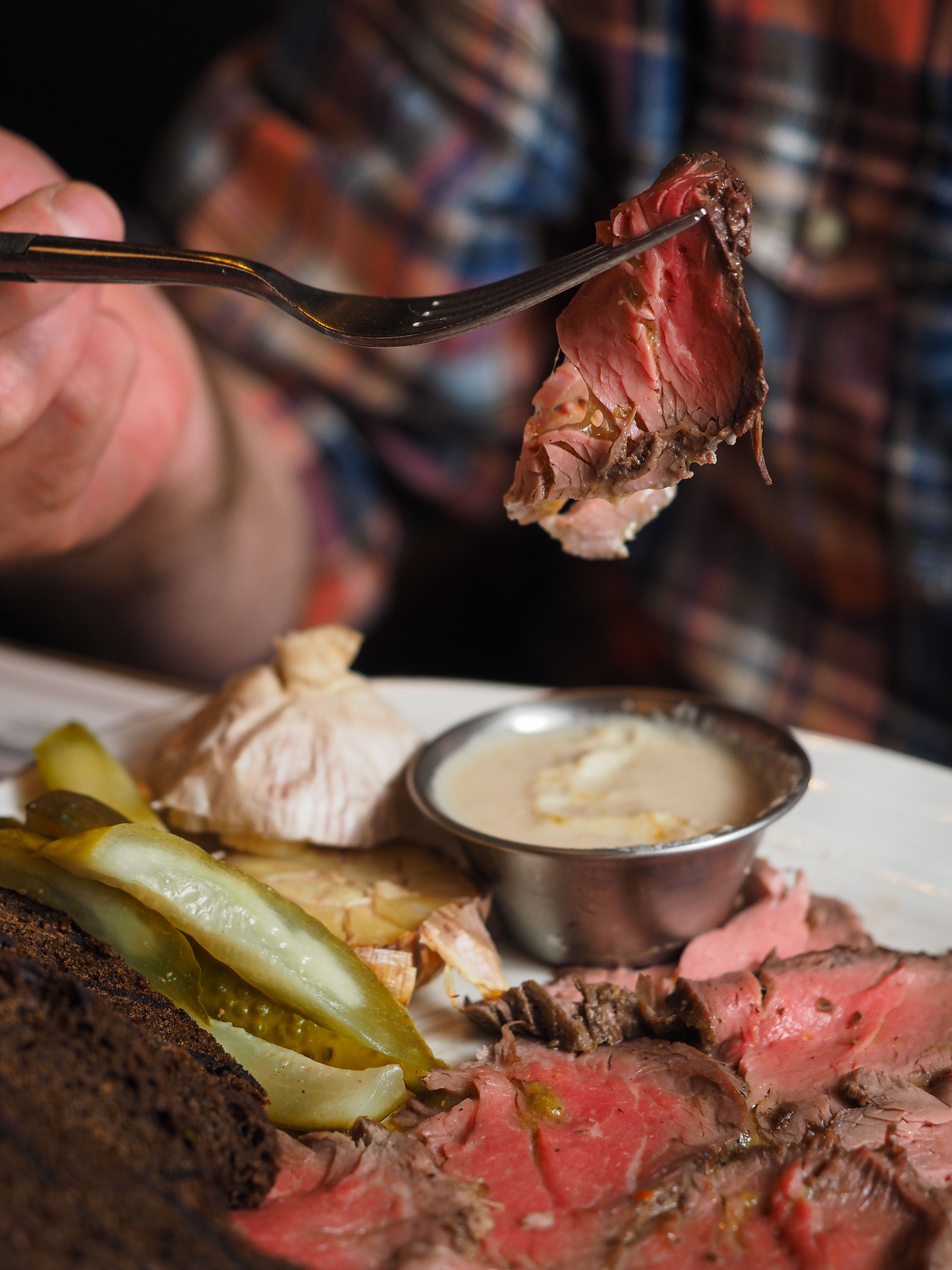 Close-up of sliced roast beef served with pickles, sauce, and brown bread in a cozy setting.