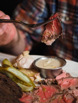 Close-up of sliced roast beef served with pickles, sauce, and brown bread in a cozy setting.