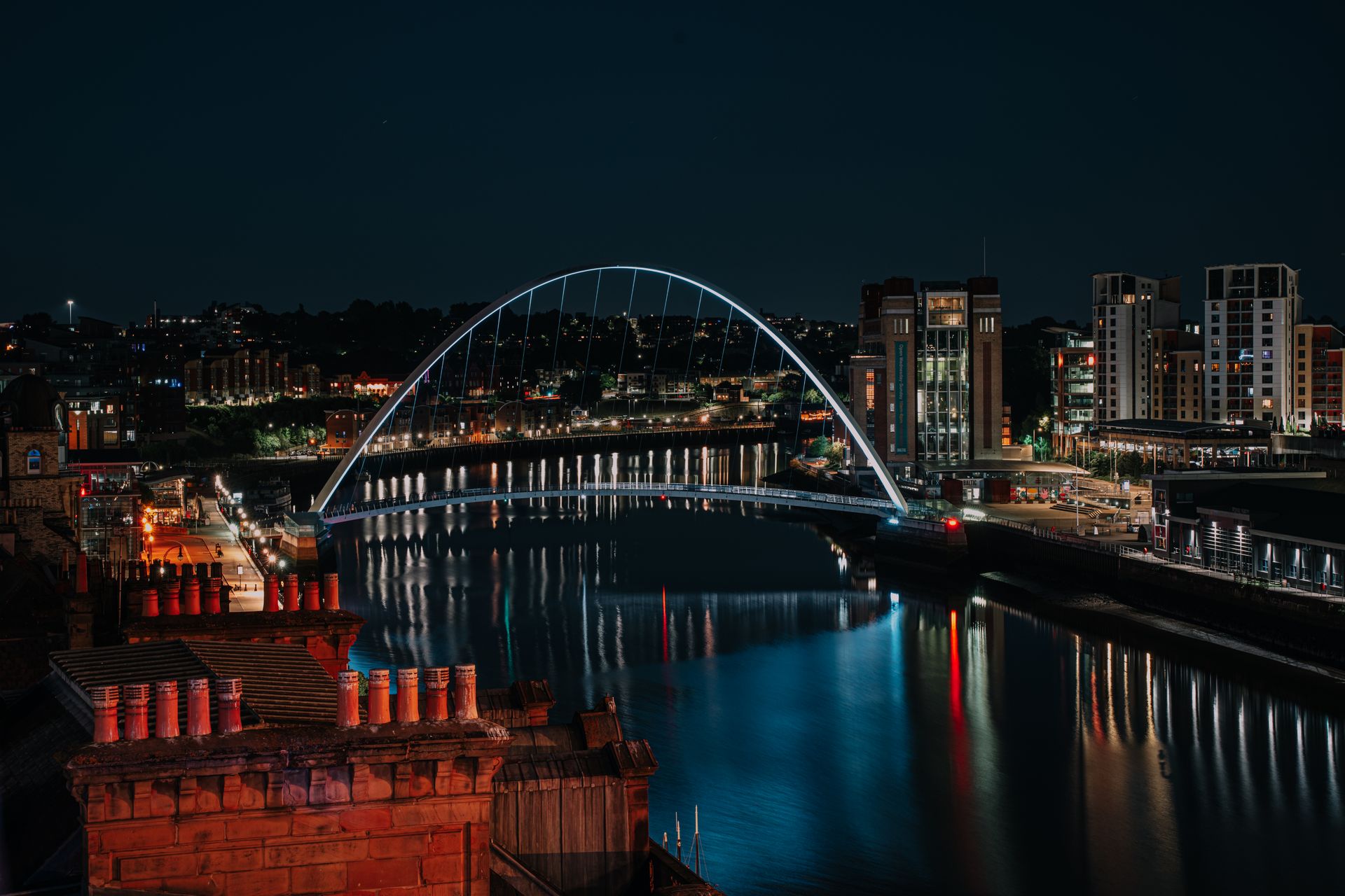 Stunning nighttime cityscape of Newcastle's Millennium Bridge reflecting in the Tyne River.