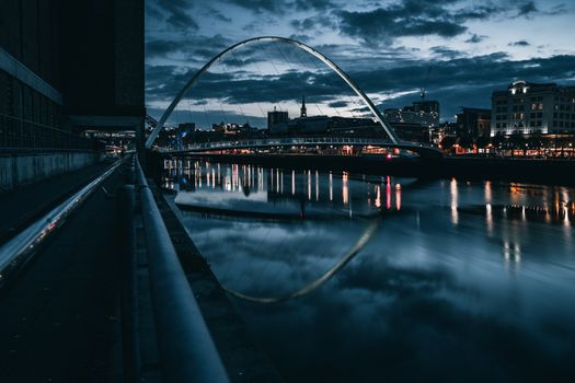A stunning night view of Gateshead Millennium Bridge with city lights reflecting on the River Tyne.