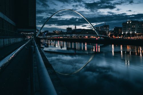 Free A stunning night view of Gateshead Millennium Bridge with city lights reflecting on the River Tyne. Stock Photo