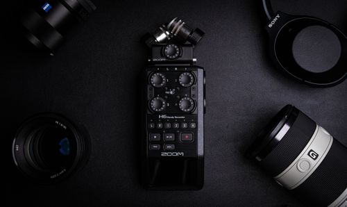 Free Top-down view of an audio recorder surrounded by camera gear on a black background. Ideal for media production themes. Stock Photo