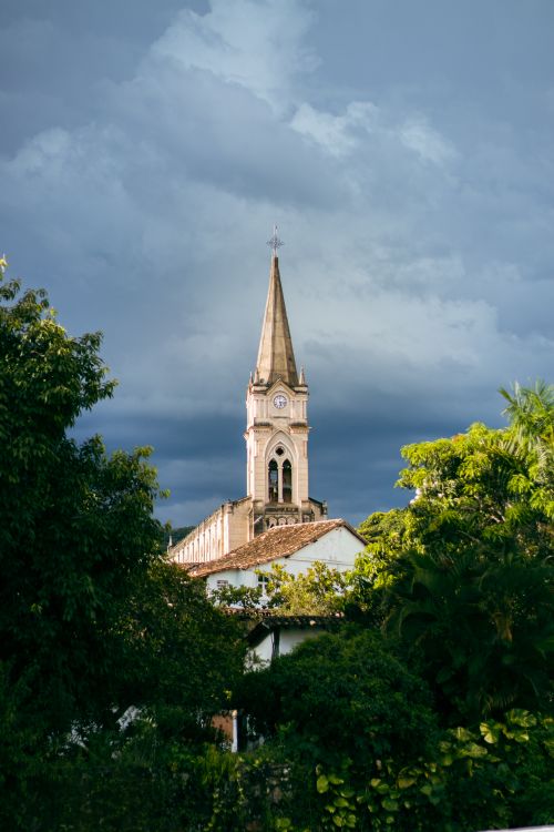 Free Dramatic sky over a historic church steeple surrounded by lush greenery in Goiás, Brazil. Stock Photo