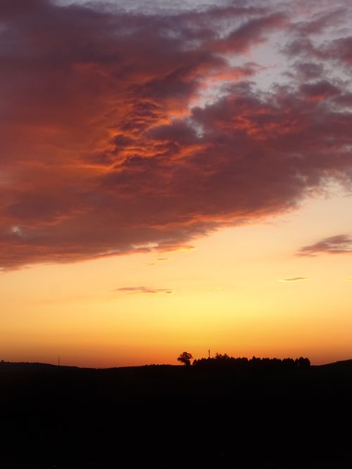 Free A breathtaking sunset featuring vibrant orange and red clouds over a silhouetted landscape. Stock Photo