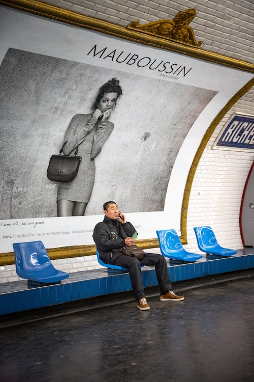 Man Sitting on Blue Chair in Front of Mauboussin Signage