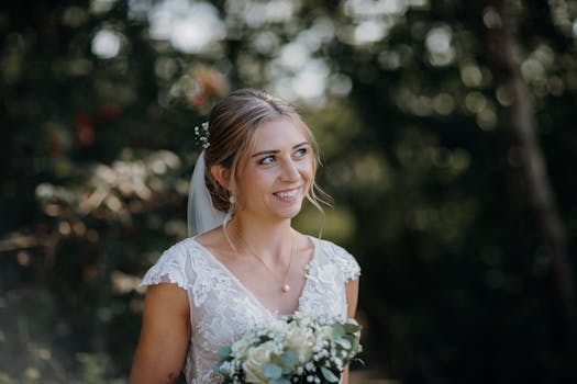A bride smiles while holding a bouquet in an outdoor wedding portrait.