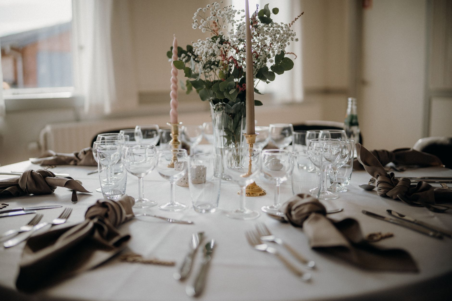A beautifully arranged wedding table setting with candles, flowers, and elegant glassware.