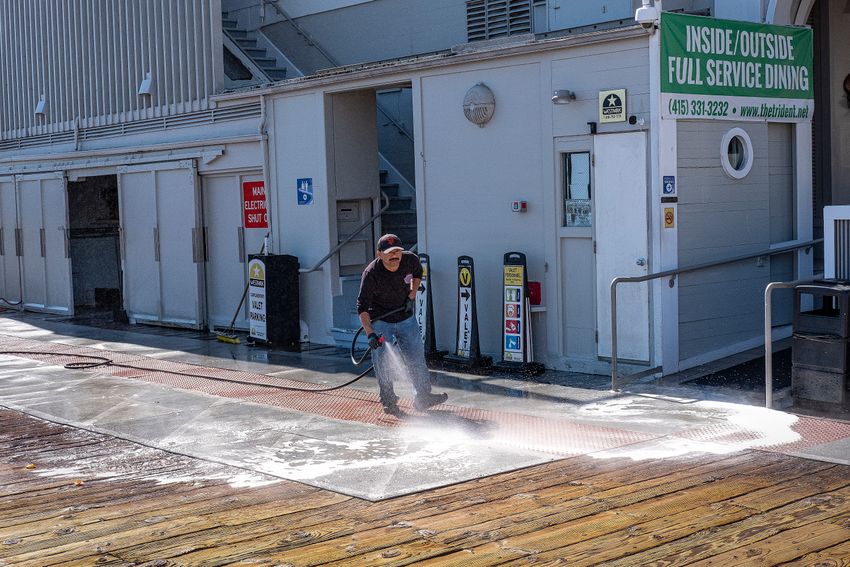 Worker pressure washing concrete sidewalk outside a commercial facility