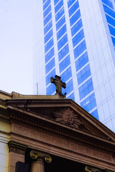 Low angle view of an old church facade with a modern skyscraper backdrop.