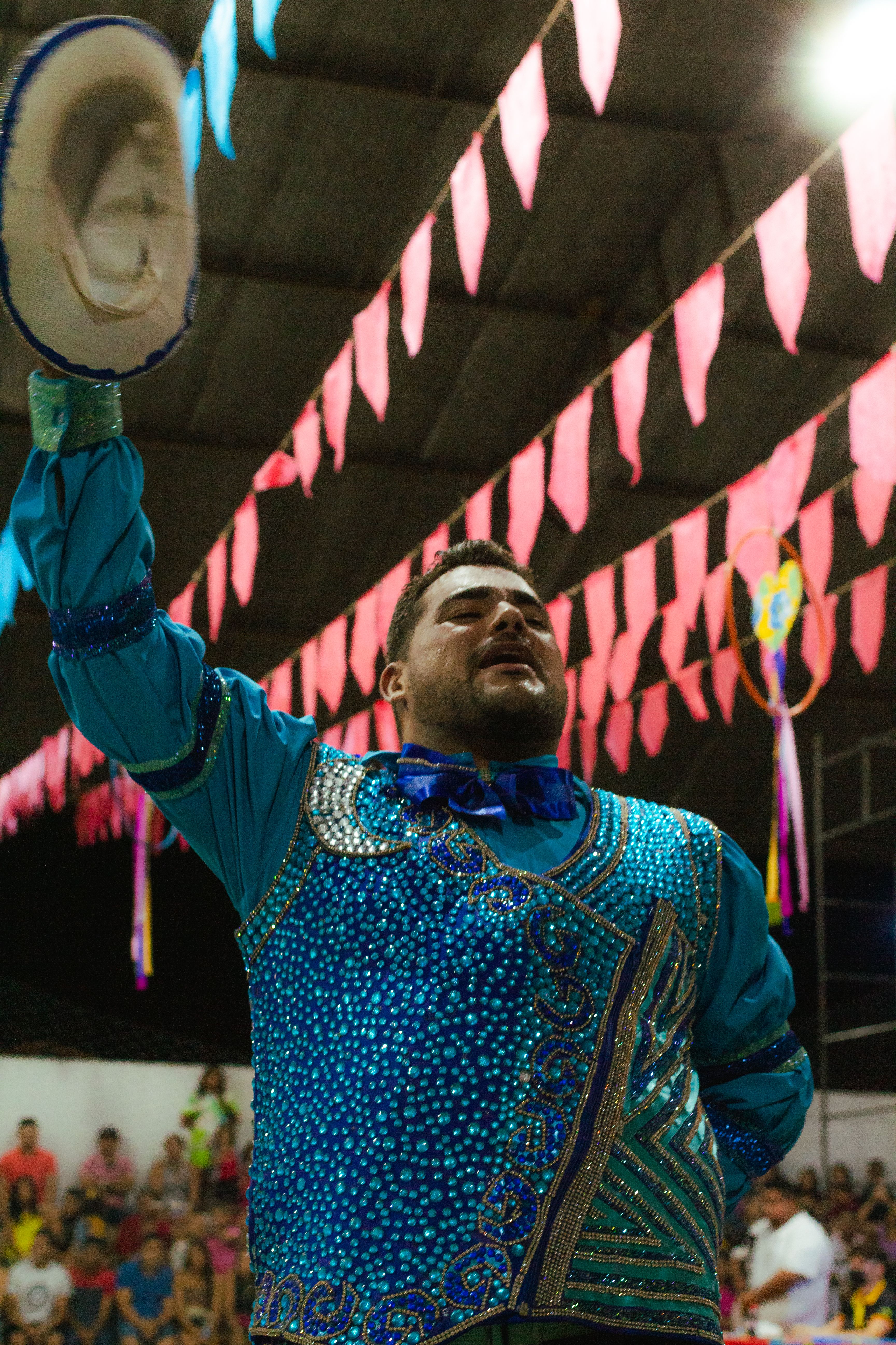 A man in vibrant traditional clothing raising a hat at a lively cultural festival.
