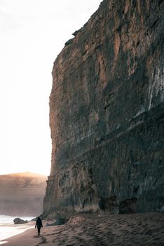 A majestic cliff by the sea during sunrise with a solitary figure walking on the sandy beach.