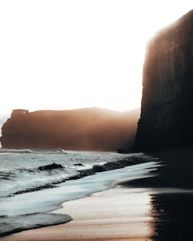 Captivating sunrise over serene beach with towering cliffs and gentle waves.
