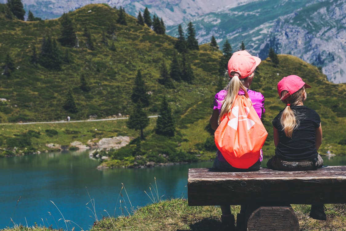 Free Two Girls Sitting on Brown Bench Near Body of Water Stock Photo