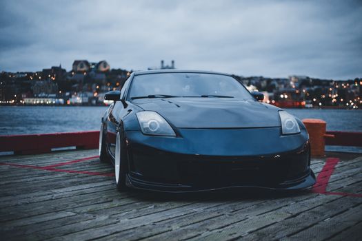 A sleek black Nissan 350Z sports car parked on a waterfront dock during twilight.