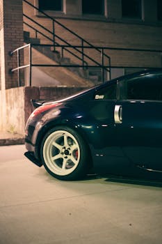 Close-up of a Nissan 350Z parked outdoors at night, emphasizing its sleek design and urban backdrop.