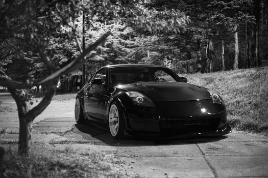 Black Nissan 350Z sports car parked along a tree-lined street at night, captured in monochrome.