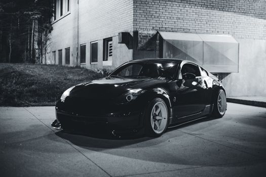 A stylish black Nissan 350Z parked by a building, captured in black and white.