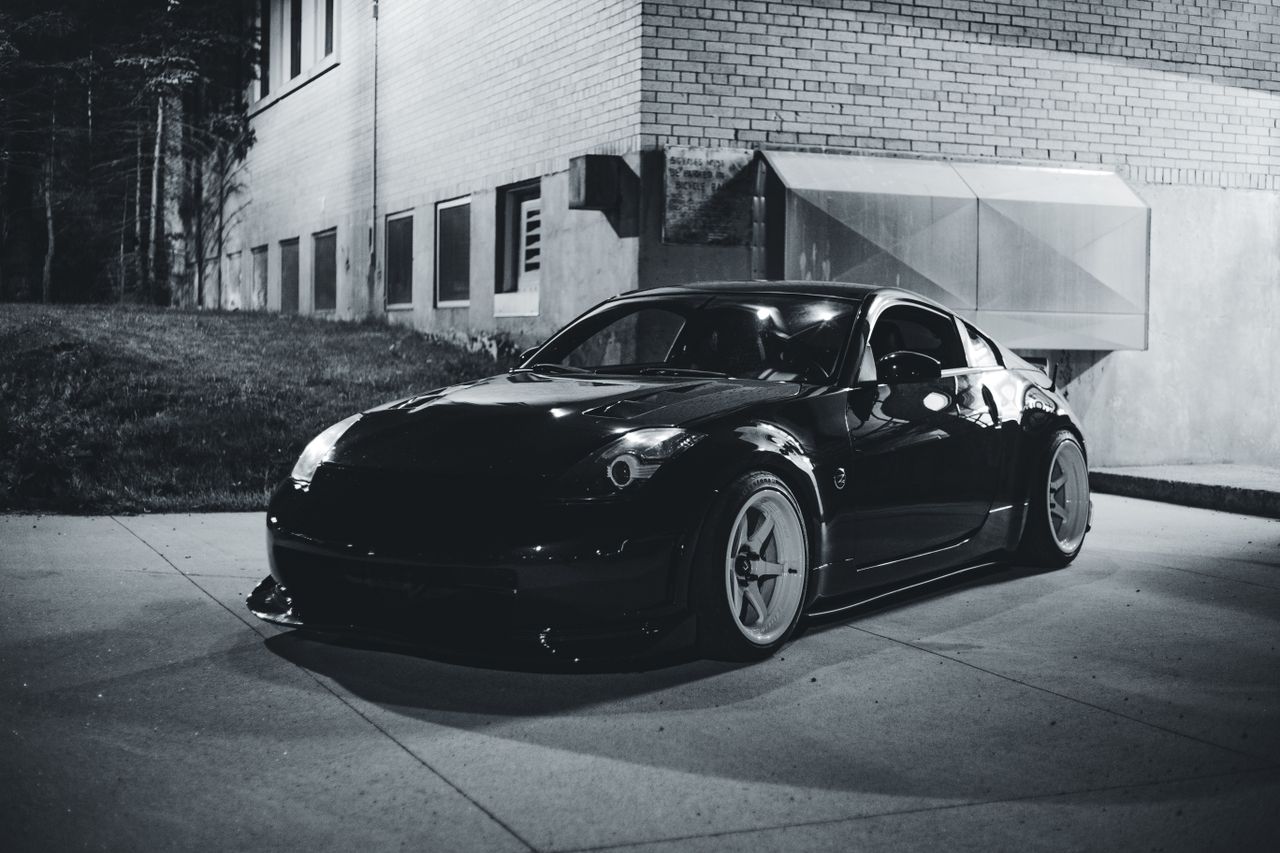 a stylish black nissan 350z parked by a building captured in black and