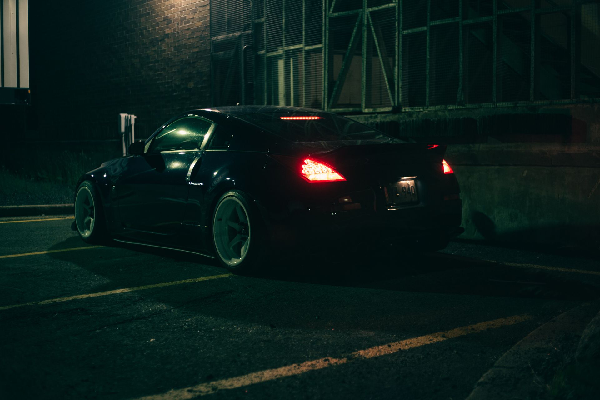 A luxury black coupe car parked at night with illuminated tail lights in an urban setting.
