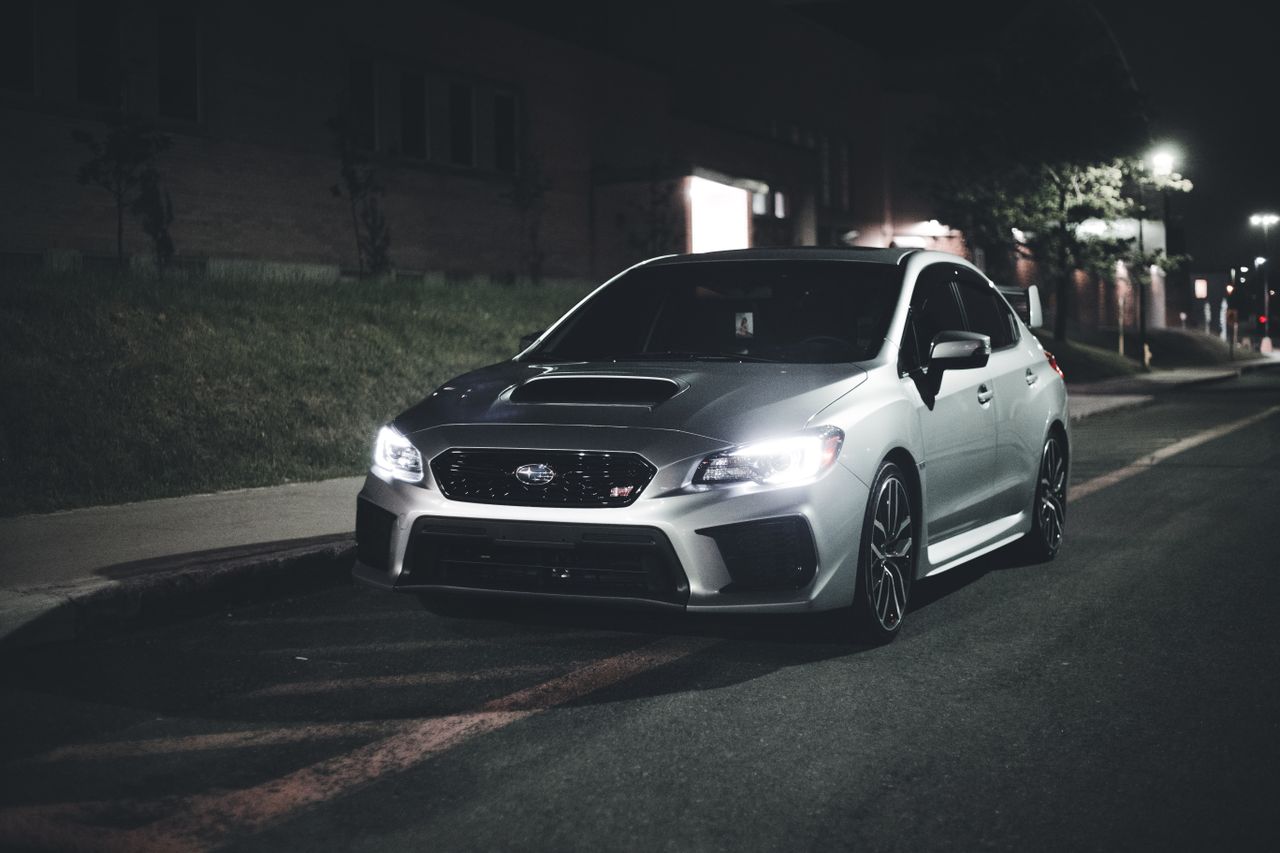 front view of a shiny silver sports car parked at night on a dimly lit