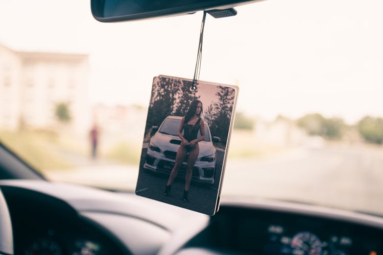 A Picture Hanging On A Rear View Mirror In The Car