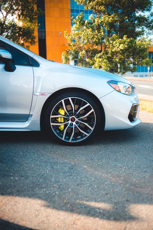 Free High-detail image of a silver car wheel on asphalt with urban backdrop and natural elements. Stock Photo