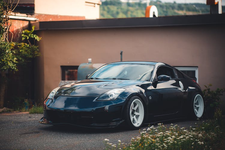 Black Nissan Car Parked Near Brown Brick Wall