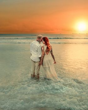A loving couple with tattoos embraces on the beach at sunset, symbolizing romance and connection.