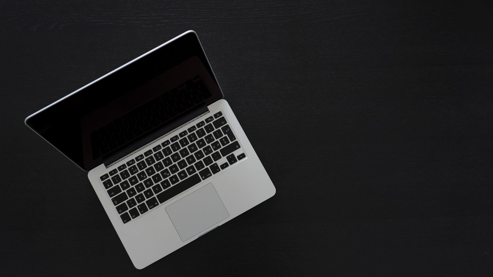 An overhead view of a single minimal laptop on a dark desk