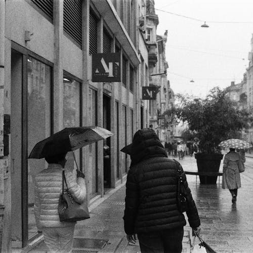 Grayscale Photo of Person in White Jacket Holding Umbrella Walking on Street
