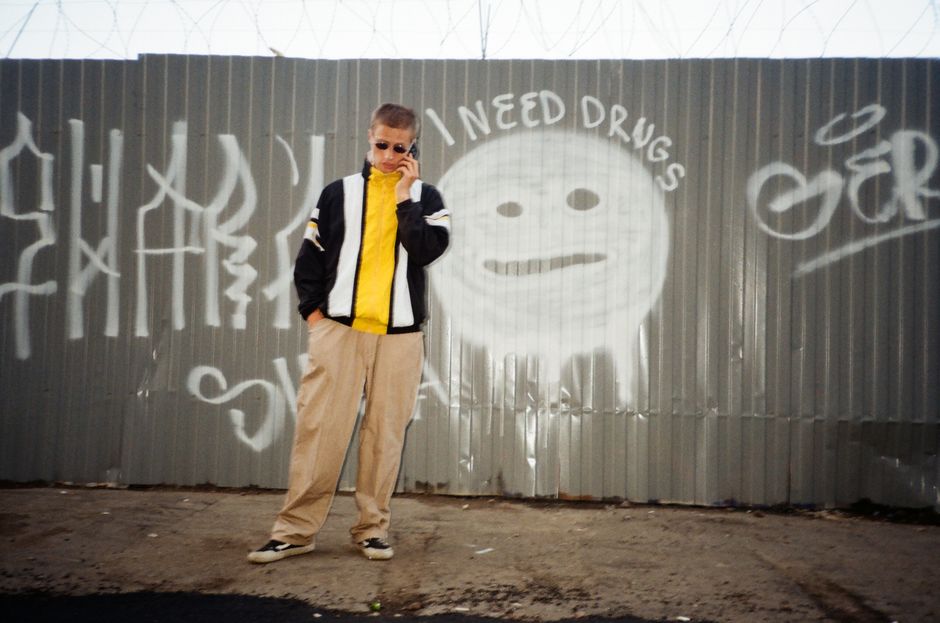 Young man in stylish outfit stands by graffiti-covered street wall, showcasing urban fashion.