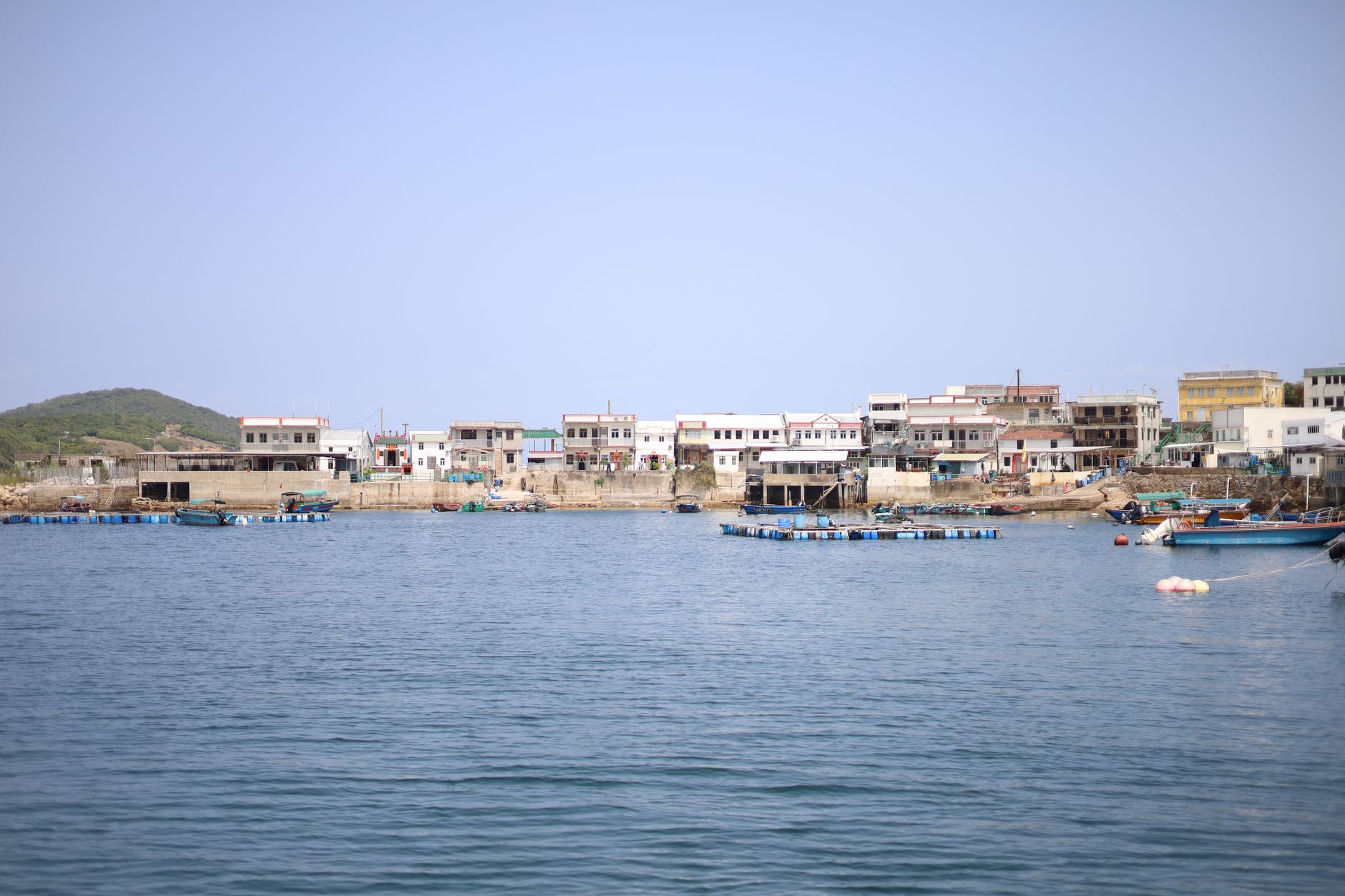 Scenic view of a fishing village along the Hong Kong coast with small boats and clear skies.