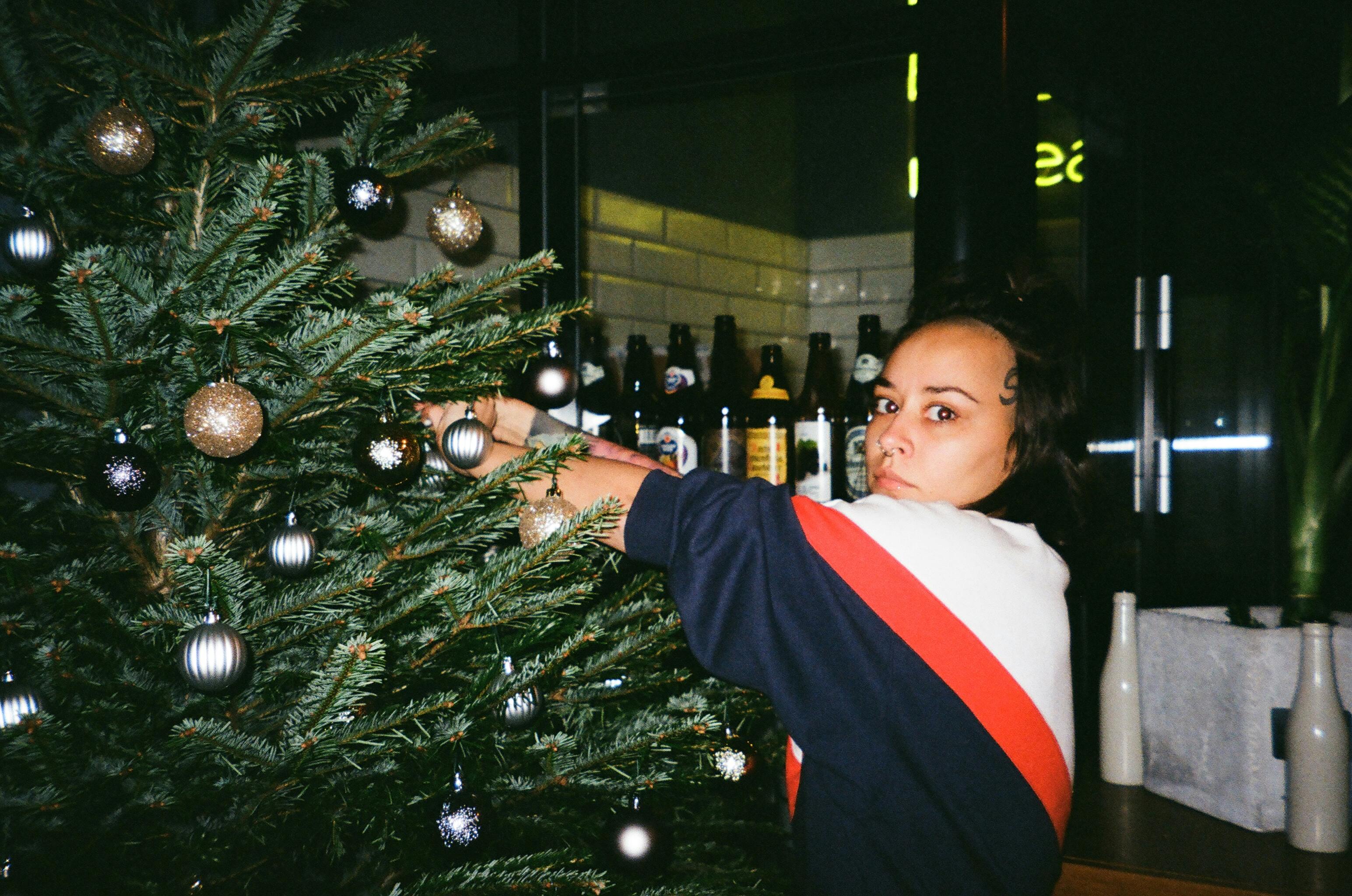 woman wearing sweater holding christmas tree with baubles inside the room