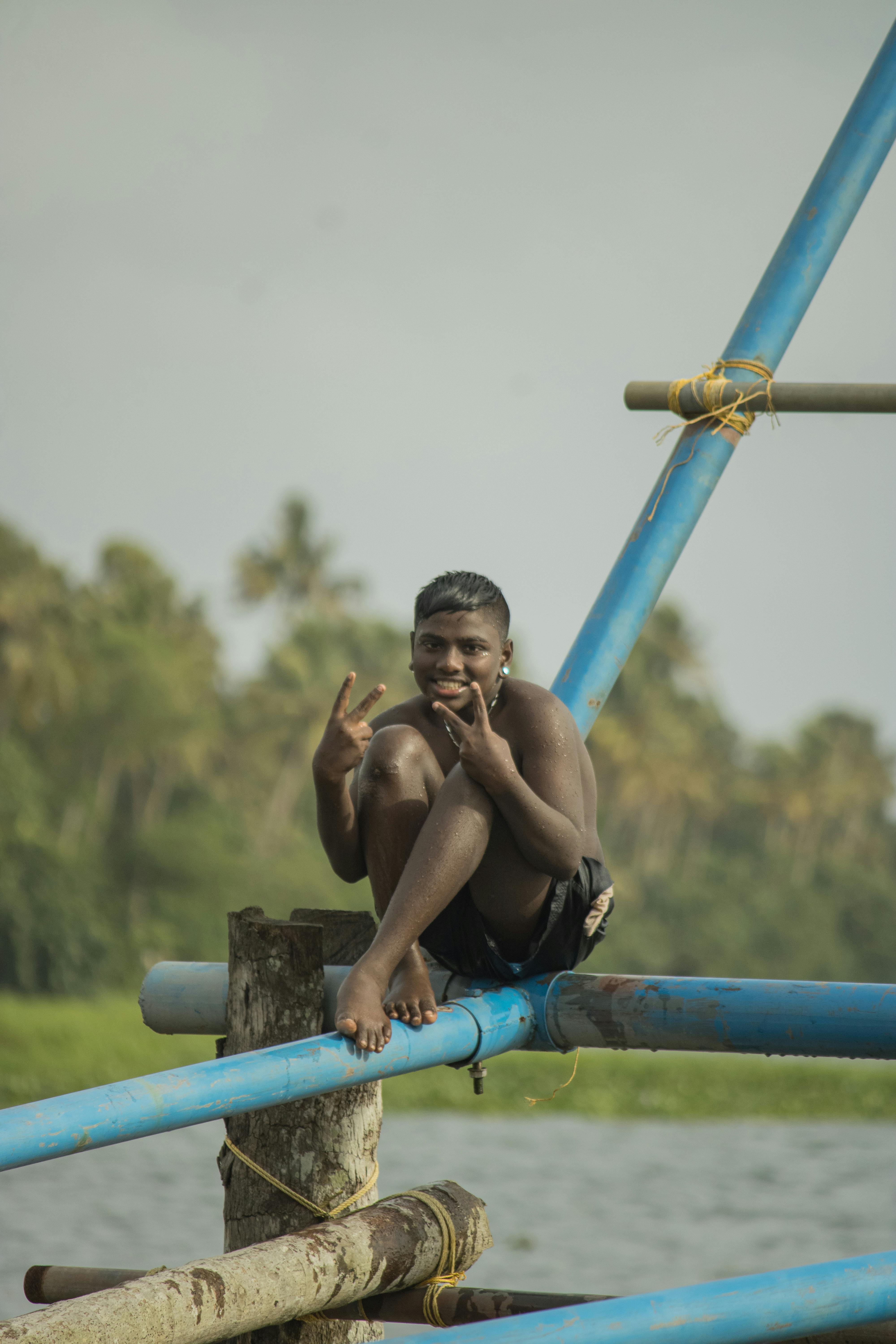 A cheerful teenager giving a peace sign while seated on a frame outdoors with nature in the background.