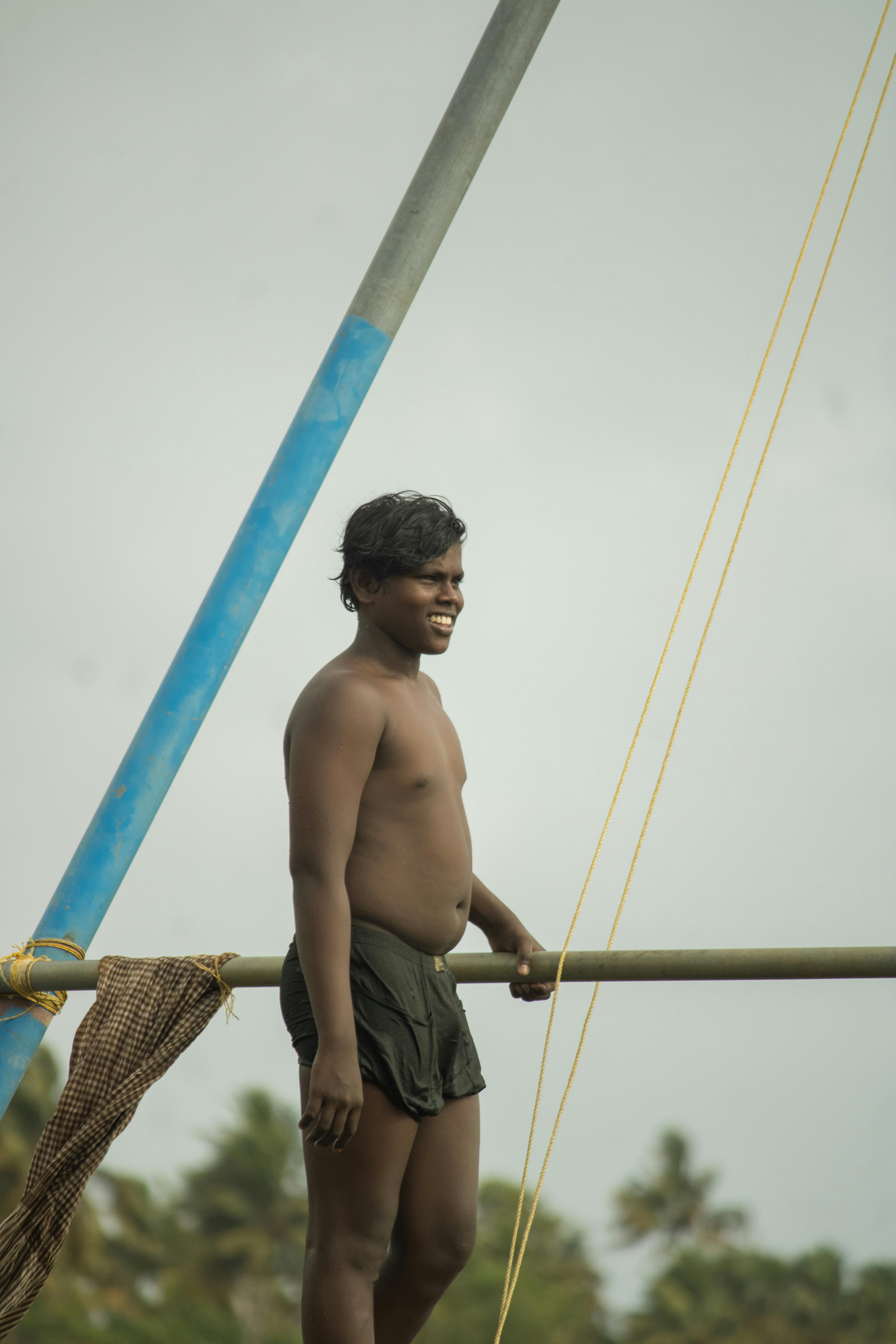 A shirtless man standing on a sturdy structure holding a fishing net outdoors.
